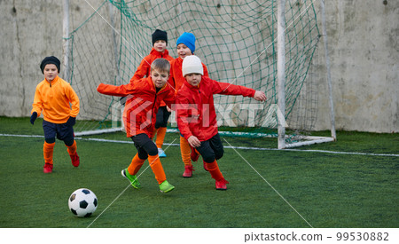 Group of boys, children, football players in uniform in motion, playing, training on field outdoors. Competition. Concept of sport, childhood, active lifestyle 99530882