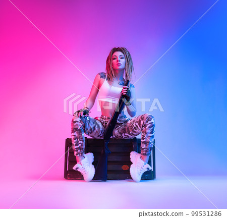 A sexy girl with braided dreadlocks on her head in neon light with a shotgun in her hands against a blank background of copy paste 99531286