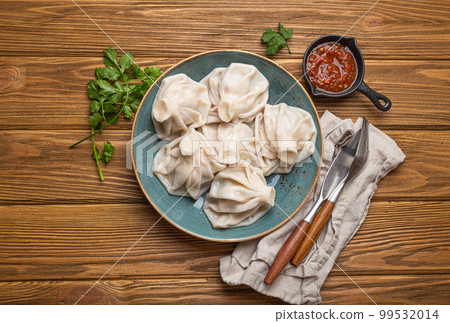 Georgian dumplings Khinkali on plate with red tomato sauce and fresh cilantro top view, rustic wooden background, traditional dish of Georgia 99532014