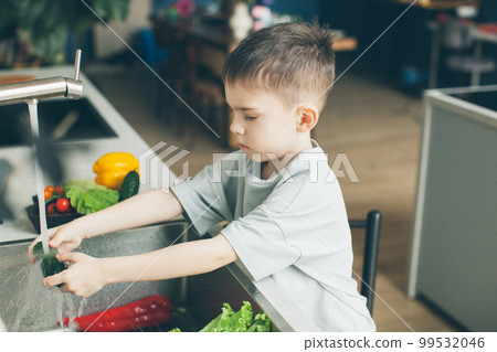 Six-year-old boy washing vegetables in the kitchen sink. Side view. 99532046