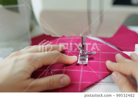 close up, woman sews clothes or accessories from pink fabric in workshop close up, woman sews clothes or accessories from pink fabric in workshop 99532482