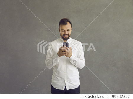 Handsome smiling man writes a message or browses social networks on a modern mobile phone. Handsome smiling man writes a message or browses social networks on a modern mobile phone. 99532892