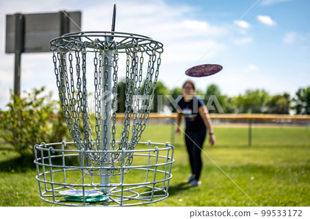 Focus on a golf hole while disc is in the air after being tossed by a defocused player Focus on a golf hole while disc is in the air after being tossed by a defocused player 99533172