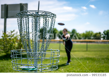 Focus on a golf hole while disc is in the air after being tossed by a defocused player Focus on a golf hole while disc is in the air after being tossed by a defocused player 99533185