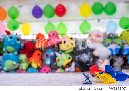 selective focus on darts sitting on a ledge with a wall of balloon targets and prizes that a player can win at a fair. selective focus on darts sitting on a ledge with a wall of balloon targets and prizes that a player can win at a fair. 99533197