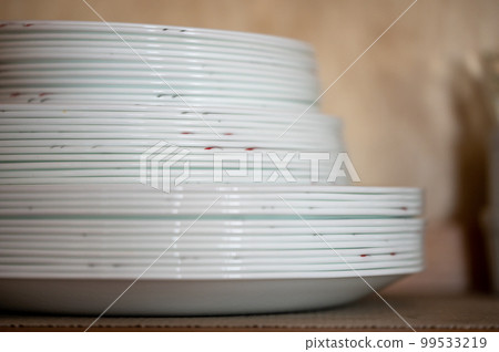 Narrow depth of field picture of an open kitchen cabinet stacked ceramic plates and bowls. 99533219