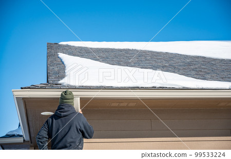 Contractor installing gutters on a residential building in the winter with snow on the roof. Contractor installing gutters on a residential building in the winter with snow on the roof. 99533224