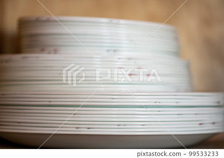 Narrow depth of field picture of an open kitchen cabinet stacked ceramic plates and bowls. 99533233