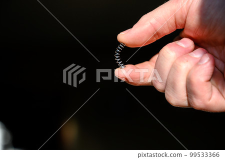 Caucasian hand compressing a metal spring between a thumb and finger Caucasian hand compressing a metal spring between a thumb and finger 99533366