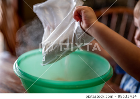 Little child dumping ingredients into a bowl causing dust to rise into the air. 99533414