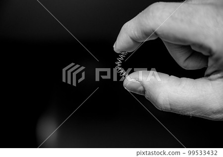 Caucasian hand compressing a metal spring between a thumb and finger Caucasian hand compressing a metal spring between a thumb and finger 99533432