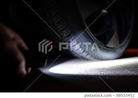 Flashlight pointing towards a vehicle flat tire at night 99533452