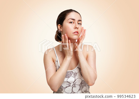 A young beautiful woman poses on a beige background, showing a healthy and well-groomed face. Copy space. The concept of cosmetology, medicine and skin care 99534623
