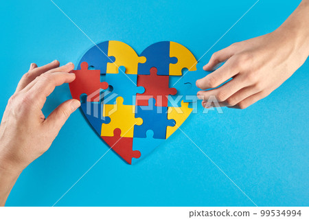 Father and autistic son hands holding jigsaw puzzle heart shape. World Autism Awareness Day 99534994