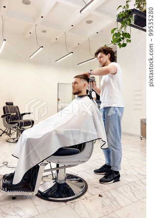 Professional hairdresser during work with man client with hair dryer 99535280