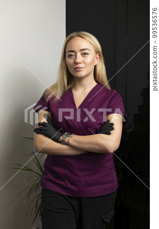 Beautiful female cosmetic physician, beauty doctor poses looking at camera, crossing hand on chests, wears medical scrubs, clothes on white black background. Cosmetology, aesthetic medicine. Vertical. Beautiful female cosmetic physician, beauty doctor poses looking at camera, crossing hand on chests, wears medical scrubs, clothes on white black background. Cosmetology, aesthetic medicine. Vertical. 99536576