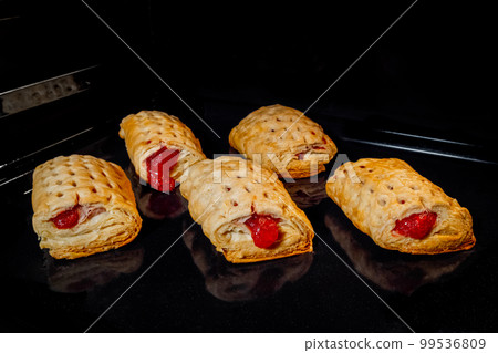 Five baked homemade buns with red strawberry jam in electric oven 99536809