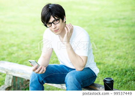 A man with glasses listening to smartphone music in a fresh green park A man with glasses listening to smartphone music in a fresh green park 99537449