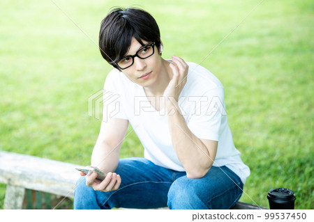 A man with glasses listening to smartphone music in a fresh green park A man with glasses listening to smartphone music in a fresh green park 99537450