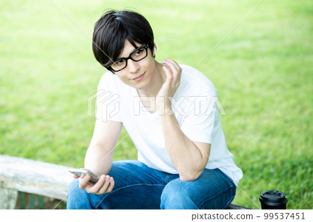 A man with glasses listening to smartphone music in a fresh green park A man with glasses listening to smartphone music in a fresh green park 99537451