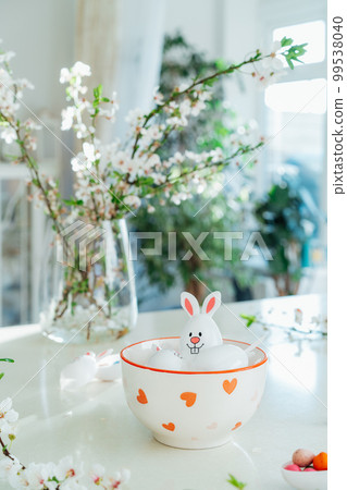 Funny Easter eggs containers with bunny ears filled with candy and chocolate in bowl on white kitchen table with blooming branches. Festive spring Easter composition. Vertical card. Selective focus Funny Easter eggs containers with bunny ears filled with candy and chocolate in bowl on white kitchen table with blooming branches. Festive spring Easter composition. Vertical card. Selective focus 99538040