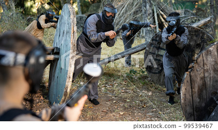 Impudent teams facing on battlefield in outdoor paintball arena during match 99539467