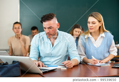 Students are retrained in the classroom of the university. Woman helping man to solve problem on laptop 99539650