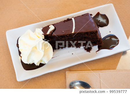 Piece of brownie cake on plate with some whipped cream and chocolate sauce Piece of brownie cake on plate with some whipped cream and chocolate sauce 99539777