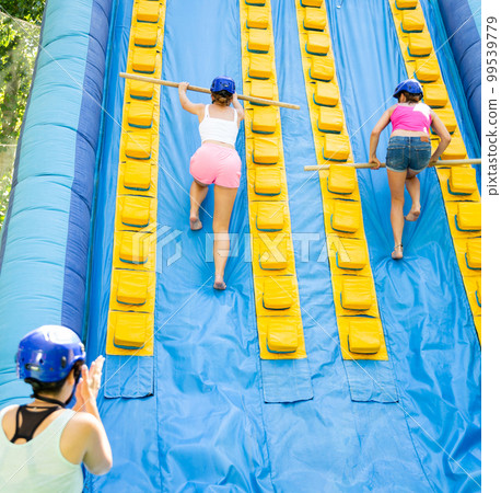 Women using sticks to reach top of slide in adventure park Women using sticks to reach top of slide in adventure park 99539779