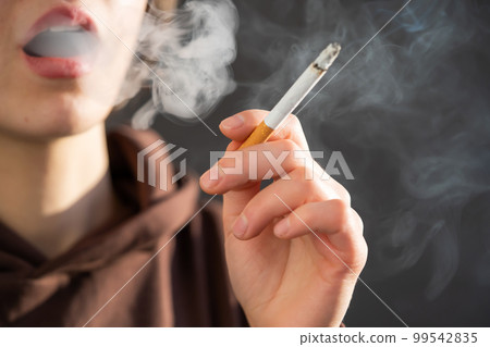 Woman is smoking, holding a cigarette in her hand. Woman is smoking, holding a cigarette in her hand. 99542835
