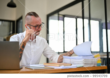 Focused Caucasian businessman with tattoo on his arms is working on financial data report Focused Caucasian businessman with tattoo on his arms is working on financial data report 99543709