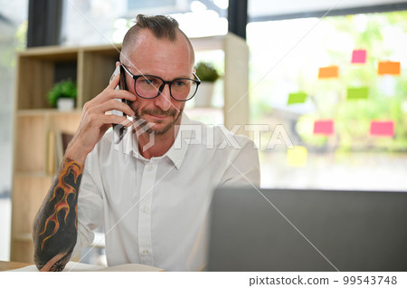 Caucasian businessman is on the phone with a client while working on project on laptop. 99543748
