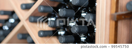 Red wine bottles stacked on wooden racks closeup 99545750