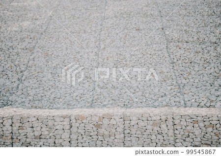 Granite stones behind a metal grate for strengthening the slope. Stones behind the wire. grey texture. construction. 99545867