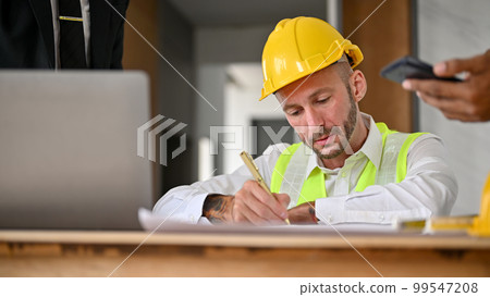Professional Caucasian male construction engineer is drawing the building's scale on a blueprint. Professional Caucasian male construction engineer is drawing the building's scale on a blueprint. 99547208