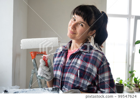 Happy woman in paint roller and white paint for walls in hands close-up portrait. Construction work and cosmetic repairs in house, wall painting, tinting, finishing work with your own hands 99547624