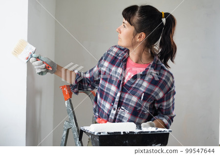 puzzled woman in paint roller and white paint for walls in hands close-up portrait. Construction work and cosmetic repairs in house, wall painting, tinting, finishing work with your own hands 99547644