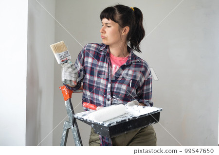 puzzled woman in paint roller and white paint for walls in hands close-up portrait. Construction work and cosmetic repairs in house, wall painting, tinting, finishing work with your own hands 99547650