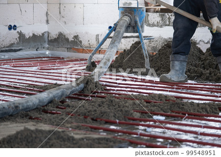 Semi-dry floor screed - a worker shovels a construction mixture through a special sleeve for cementing and leveling on underfloor heating pipes. Semi-dry floor screed - a worker shovels a construction mixture through a special sleeve for cementing and leveling on underfloor heating pipes. 99548951
