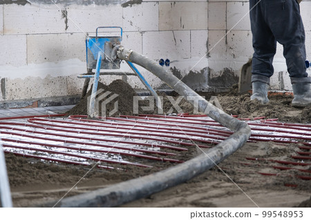 Semi-dry floor screed - a worker shovels a construction mixture through a special sleeve for cementing and leveling on underfloor heating pipes. Semi-dry floor screed - a worker shovels a construction mixture through a special sleeve for cementing and leveling on underfloor heating pipes. 99548953