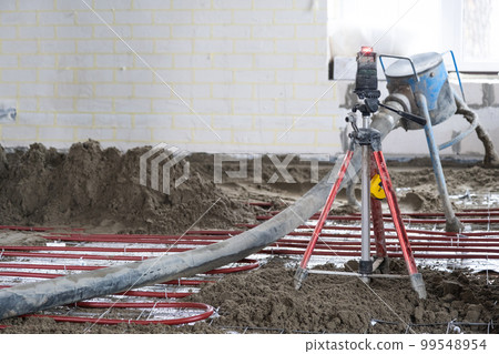 Semi-dry floor screed - a worker shovels a construction mixture through a special sleeve for cementing and leveling on underfloor heating pipes. 99548954