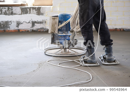 Ramming and grinding of semi-dry floor screed by a machine with a rotating disk for leveling. Construction of a concrete floor in the house, a master with special equipment. Ramming and grinding of semi-dry floor screed by a machine with a rotating disk for leveling. Construction of a concrete floor in the house, a master with special equipment. 99548964