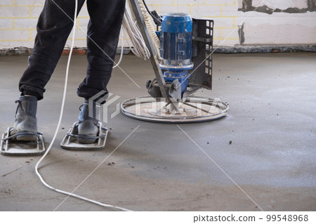 Ramming and grinding of semi-dry floor screed by a machine with a rotating disk for leveling. Construction of a concrete floor in the house, a master with special equipment. 99548968
