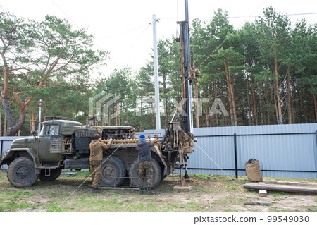Team of workers with drilling rig on car are drilling artesian well for water in ground. Insertion of metal casing pipe into ground, installation of individual drinking supply, June 28, 2022, Russia, Team of workers with drilling rig on car are drilling artesian well for water in ground. Insertion of metal casing pipe into ground, installation of individual drinking supply, June 28, 2022, Russia, 99549030