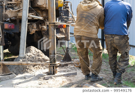 Team of workers with drilling rig on car are drilling artesian well for water in ground. Insertion of metal casing pipe into ground, installation of individual drinking supply, June 28, 2022, Russia, 99549176