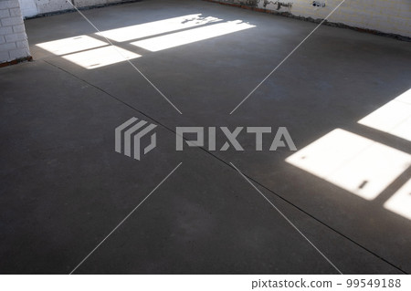 The leveled rough floor in a house under construction with a semi-dry cement screed is a smooth surface with light from the windows The leveled rough floor in a house under construction with a semi-dry cement screed is a smooth surface with light from the windows 99549188