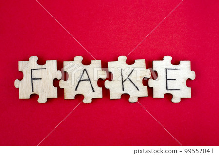 Learning FAKE. The hand lettering on the wooden puzzles is insulated on a white background. The word written on wooden puzzles lying on a red background 99552041