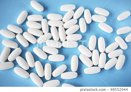 L glutamine white oval tablets scattered on a blue background, view from above 99552044