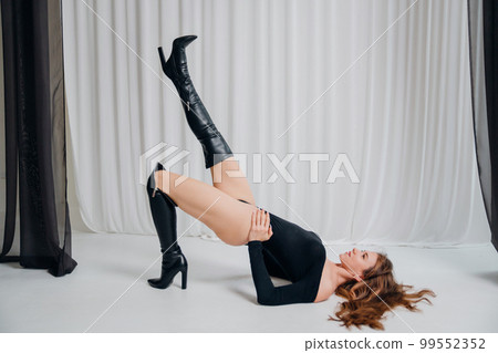 a beautiful sexy slender woman in a black bodysuit and boots poses on the floor. 99552352