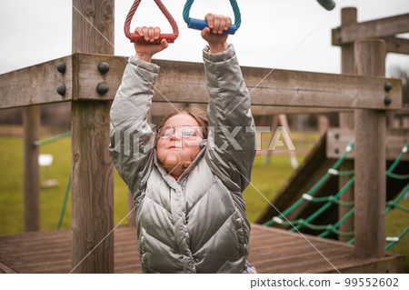 Primary school happy funny girl plays in the playground. A child does sports exercises while claiming. Child in glasses hold on. Health and education. Primary school happy funny girl plays in the playground. A child does sports exercises while claiming. Child in glasses hold on. Health and education. 99552602